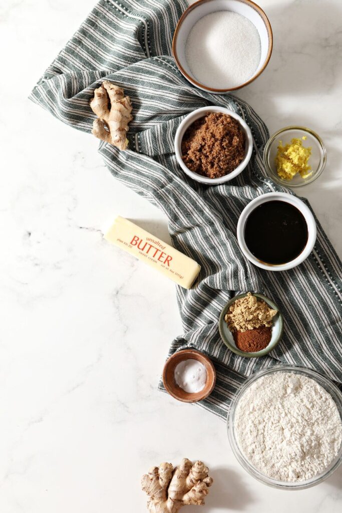 Ingredients to make ginger snaps on a marble background with a dark green striped towel