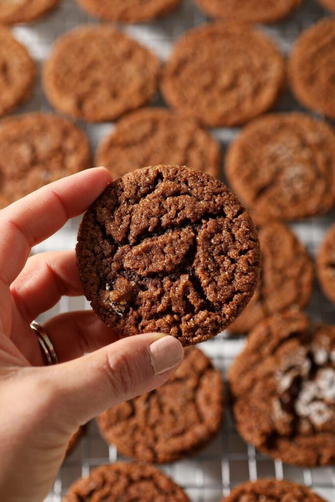 A hand holds a gingersnap above a cooling rack of many