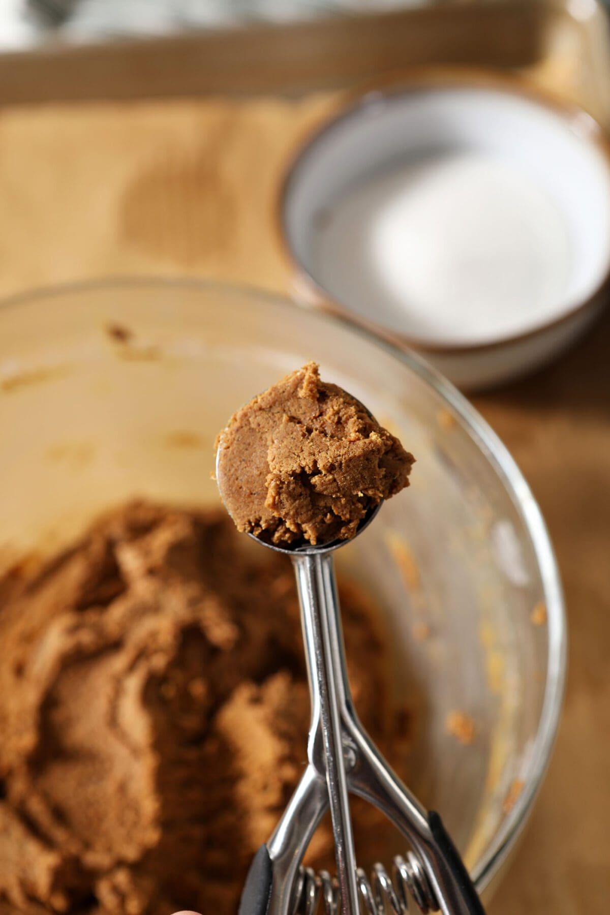 A cookie scoop of ginger snap cookie dough above a bowl