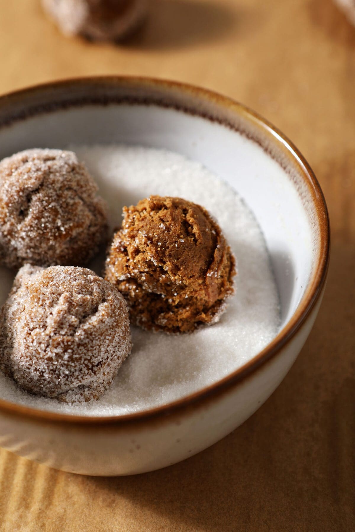 Three scoops of ginger snap cookie dough in a bowl of granulated sugar