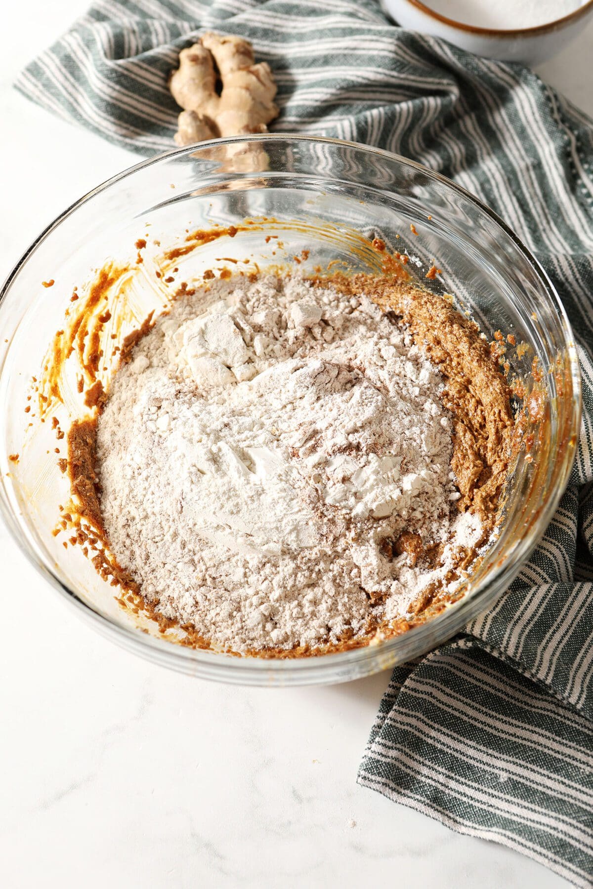 The dry ingredients sprinkled on top of wet ingredients for gingersnaps in a bowl on marble