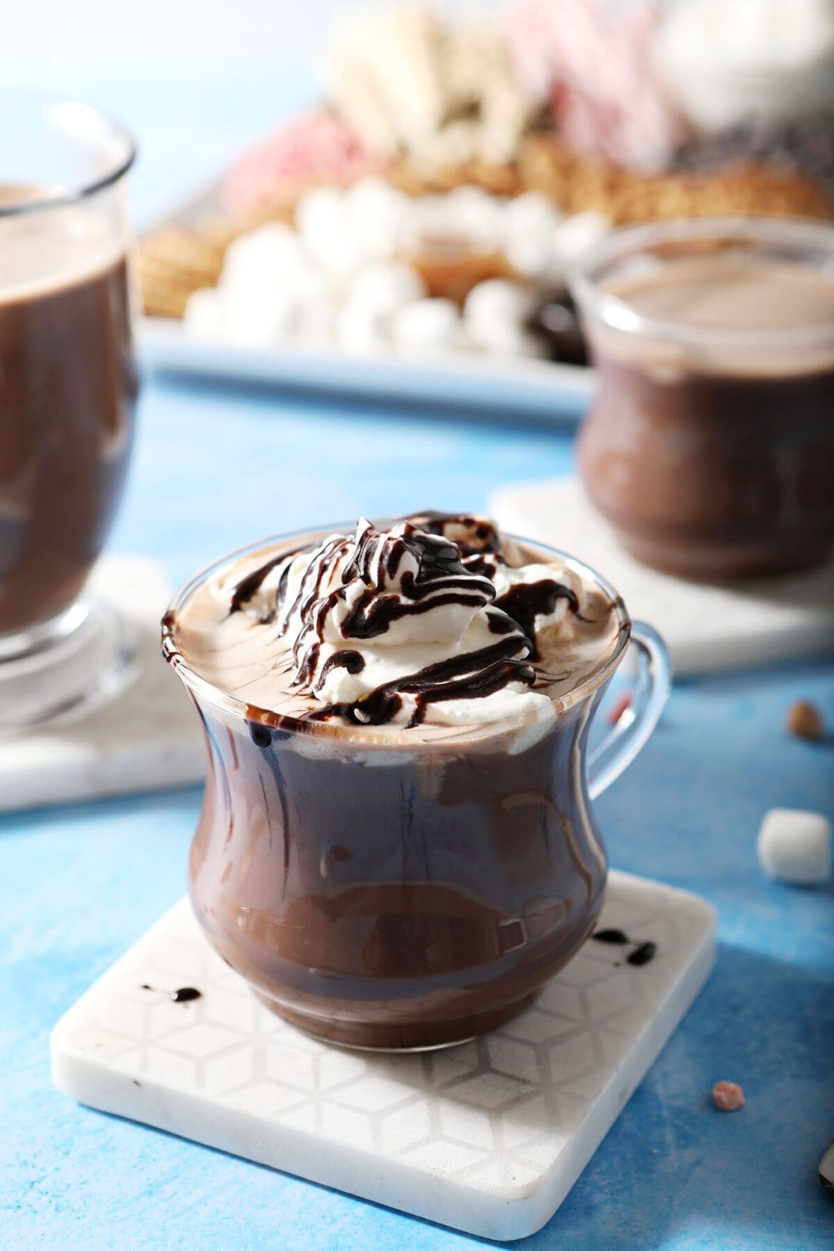 A mug of cocoa with two others by a hot cocoa board