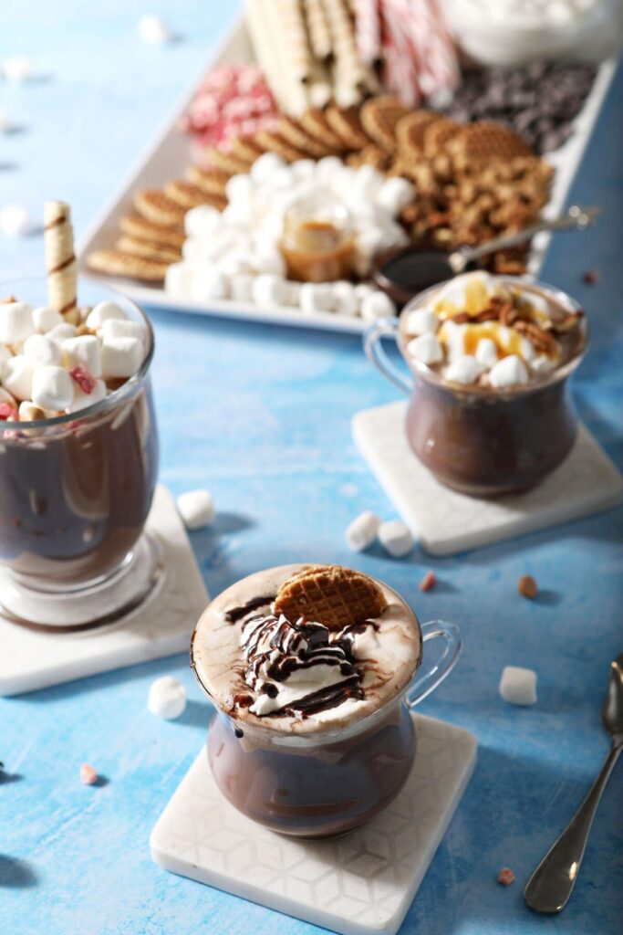 Three mugs of hot chocolate next to a hot cocoa board