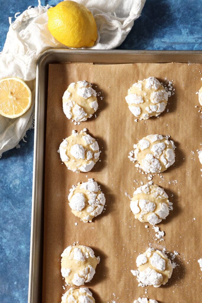 A cookie sheet lined with parchment with lemon crinkle cookies on it