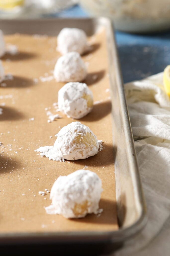 Lemon Crinkle Cookie dough rolled in powdered sugar before baking on a sheet pan