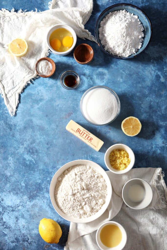 Ingredients to make lemon crackle cookies on a blue countertop with white tea towels