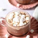 Close up of a mug of slow cooker hot cocoa topped with mini marshmallows on a pink plate