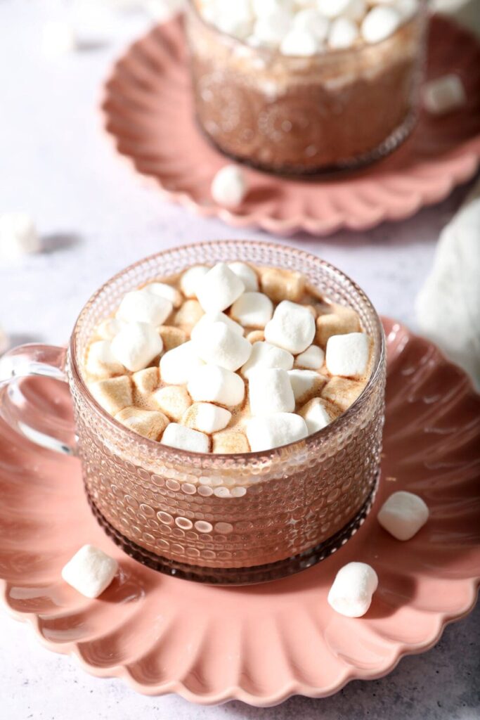 Close up of a mug of slow cooker hot cocoa topped with mini marshmallows on a pink plate