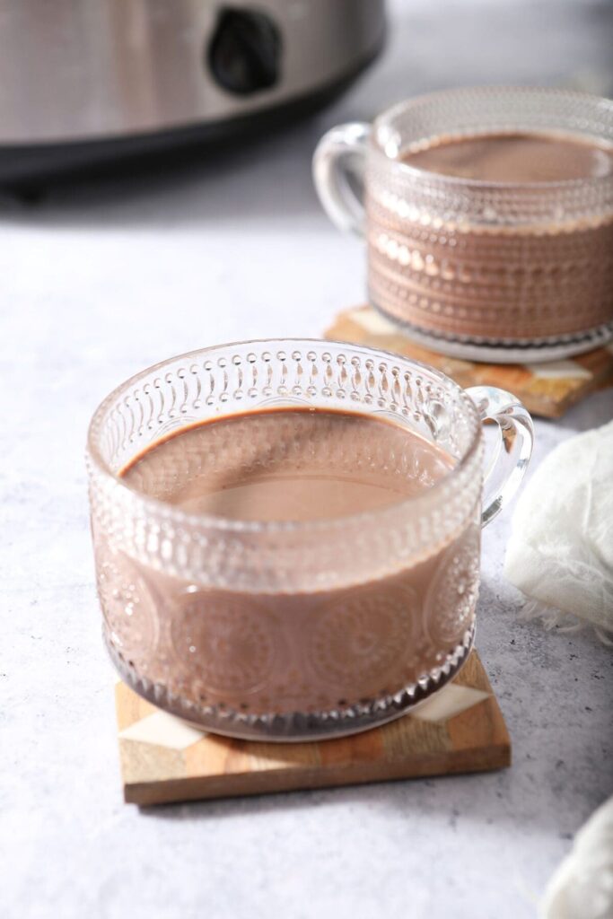 Two clear mugs of homemade Hot Cocoa on wooden coasters