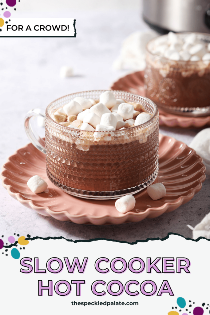 Two glass mugs of hot cocoa topped with mini marshmallows on pink plates with the text Slow Cooker Hot Cocoa for a crowd