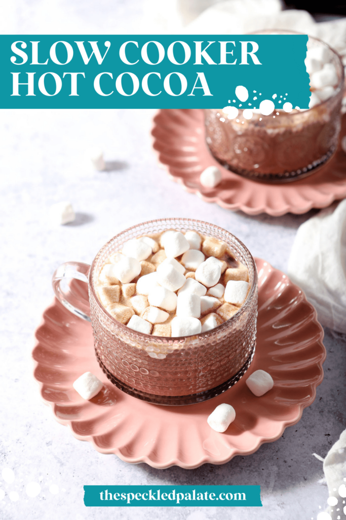 Two glass mugs of hot cocoa topped with mini marshmallows on pink plates with the text Slow Cooker Hot Cocoa