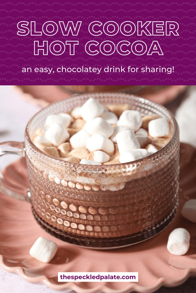 Close up of a glass mug of hot cocoa topped with mini marshmallows on a pink plate with the text How to make Slow Cooker Hot Cocoa an easy chocolatey drink for sharing