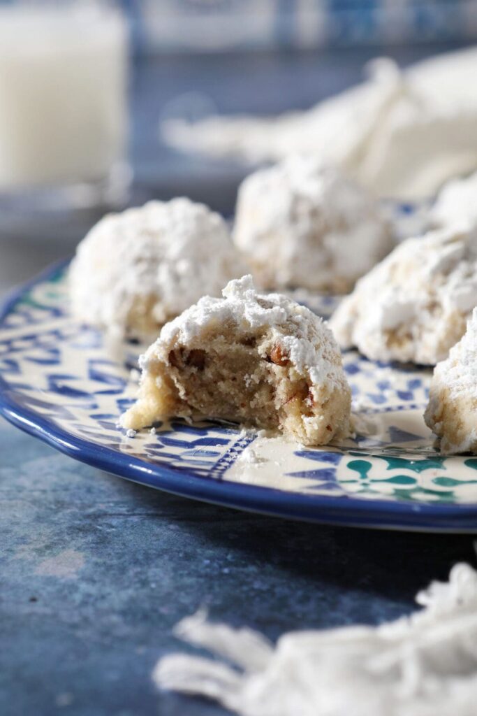 A blue plate of snowball cookies with one cookie with a bite taken out of it