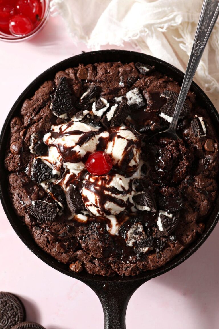 A spoon scoops into a Oreo skillet brownie topped with ice cream, chocolate sauce and a cherry