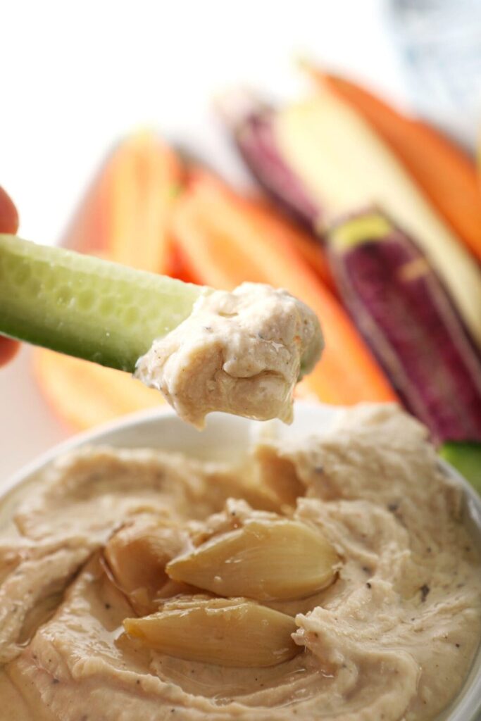 A cucumber slice dips into Roasted Garlic White Bean Hummus