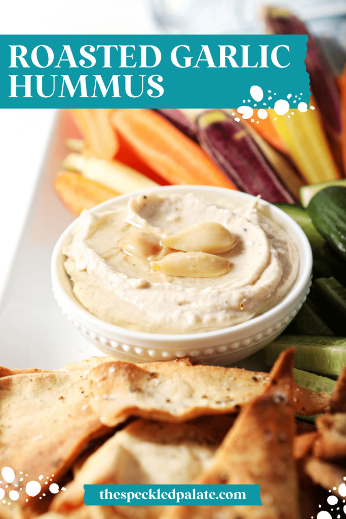 A serving bowl of hummus surrounded by homemade pita chips, cucumbers and carrots with the text Roasted Garlic Hummus