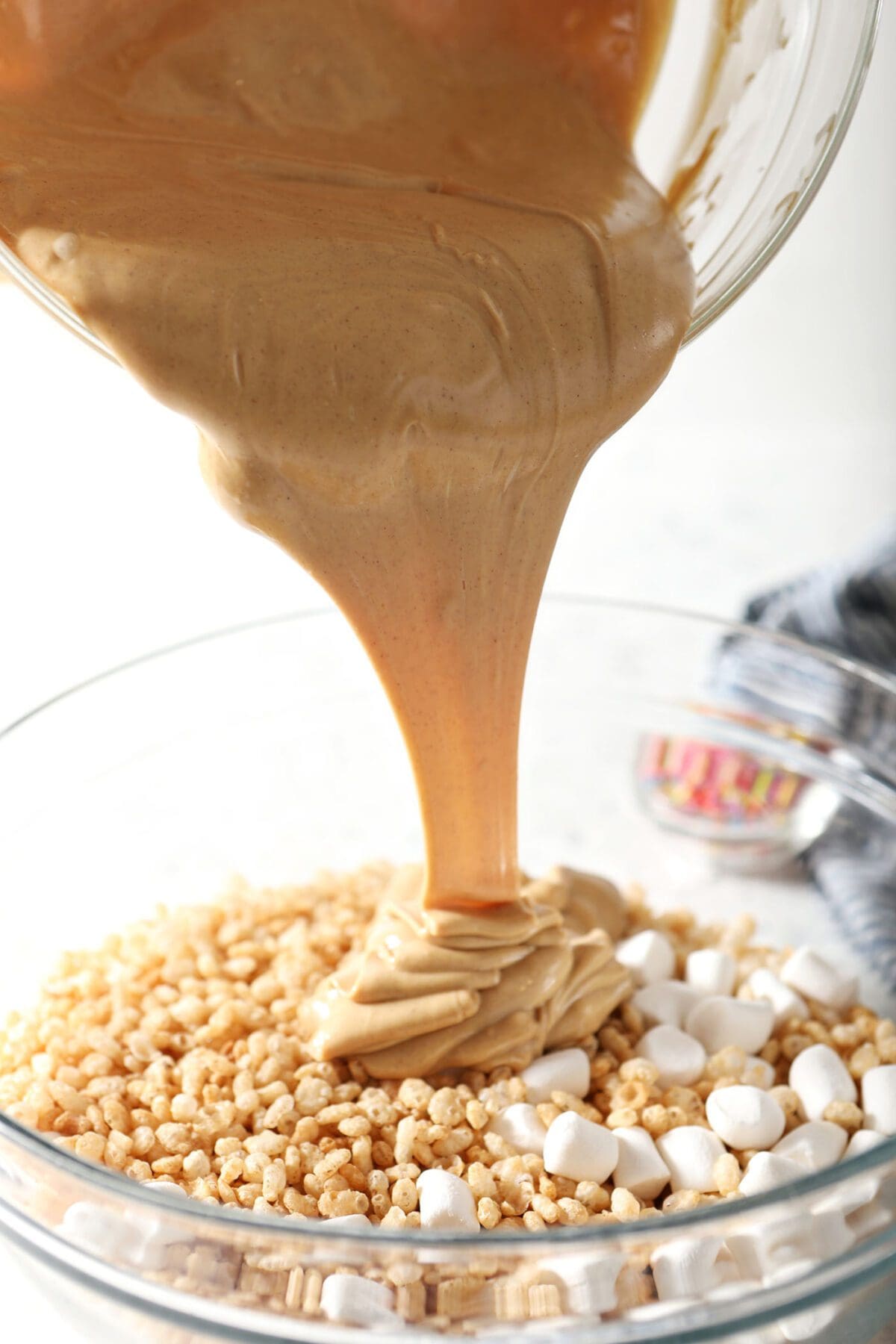 The peanut butter-white chocolate mixture pours on top of Rice Krispies and marshmallows in a bowl