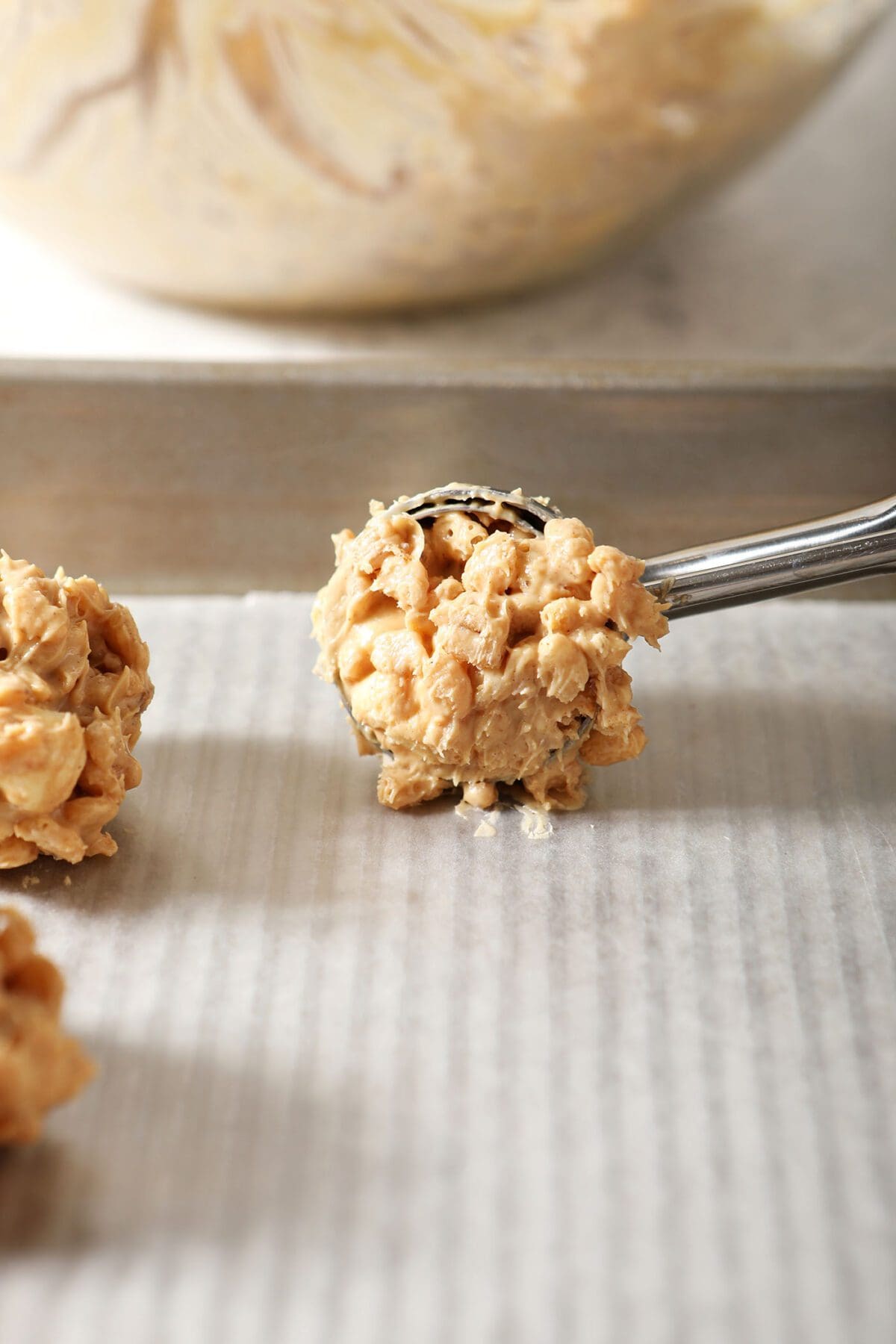 A cookie scoop drops an avalanche cookie on a sheet pan