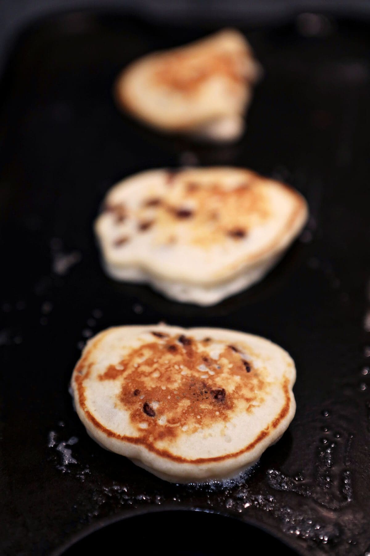 Three flipped Chocolate Chip Pancakes on a griddle