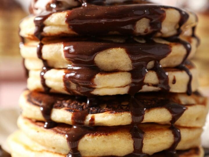Close up of chocolate sauce drizzling down a tall stack of Chocolate Chip Pancakes