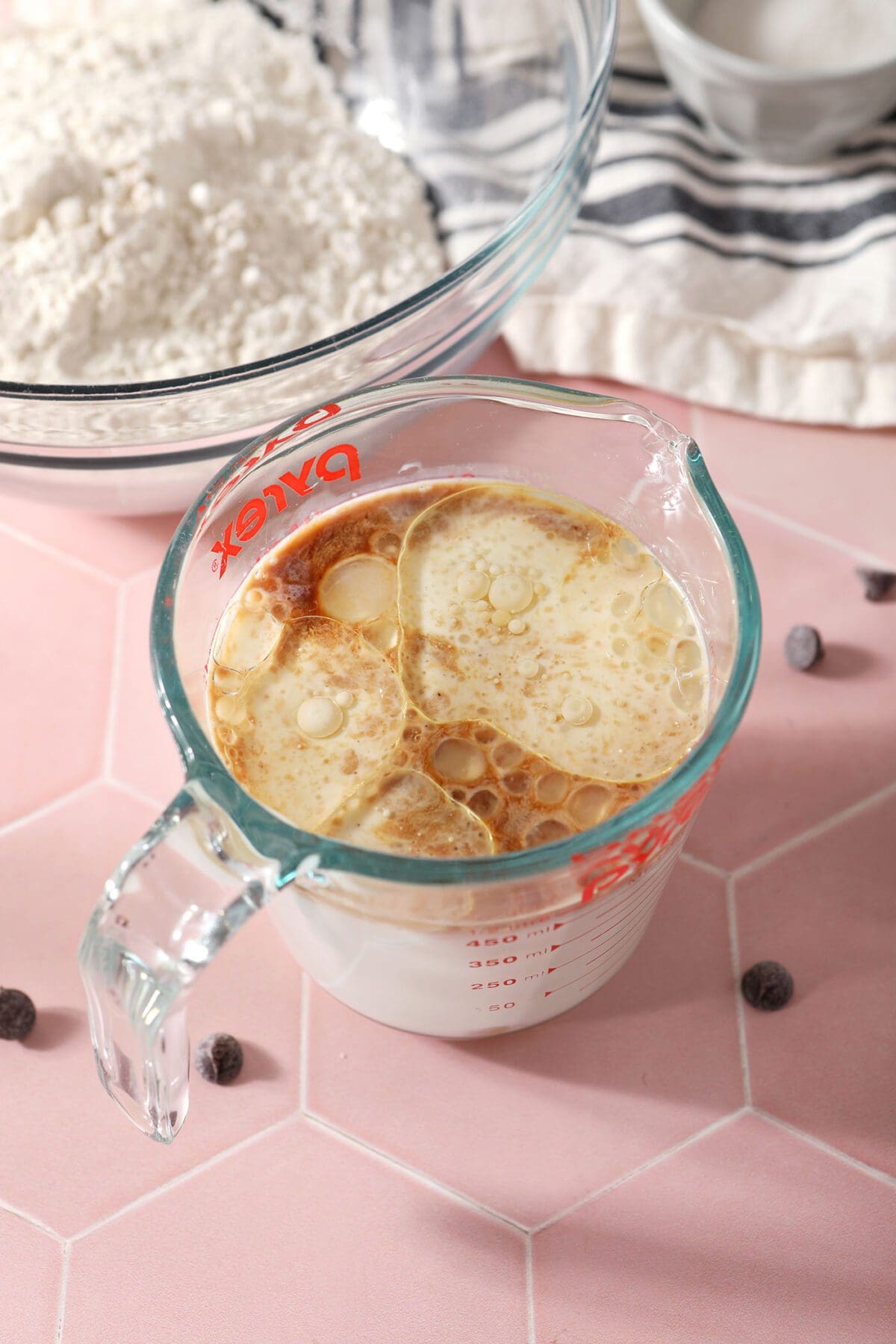 Wet ingredients in a liquid measuring cup on a pink tile countertop