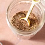 Creole seasoning in a jar with a teaspoon in the jar on a red tile