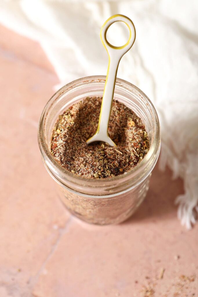 A teaspoon sits in a mason jar full of a homemade creole spice blend