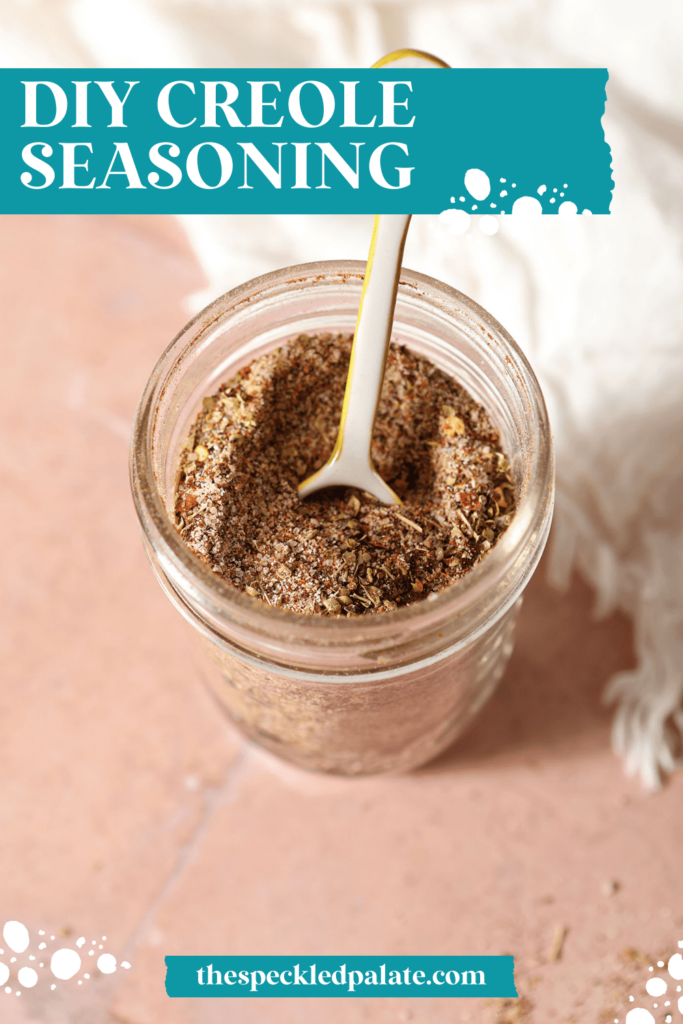 Closeup of a teaspoon in a homemade spice blend in a mason jar with the text DIY Creole Seasoning