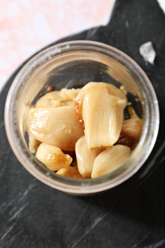 Roast garlic cloves in a jar on a black marble cutting board