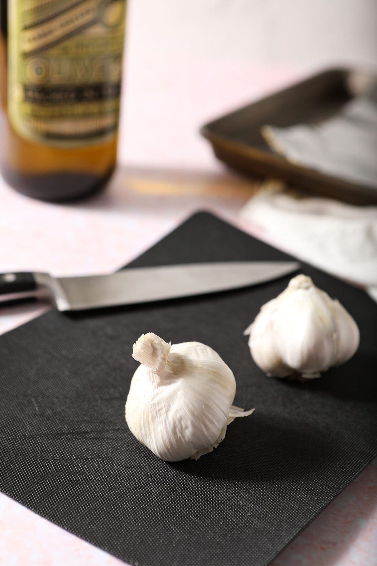 Two cloves of garlic on a black cutting board with a knife