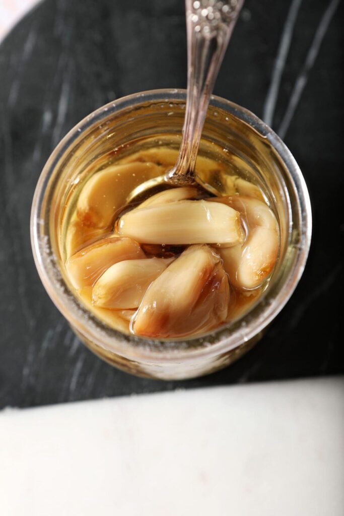 Roasted garlic cloves in a jar with a spoon and oil