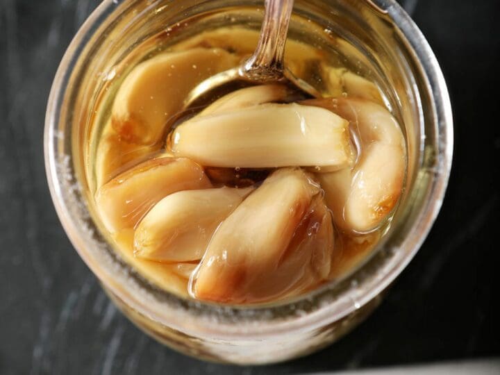 Roasted garlic cloves in a jar with a spoon and oil