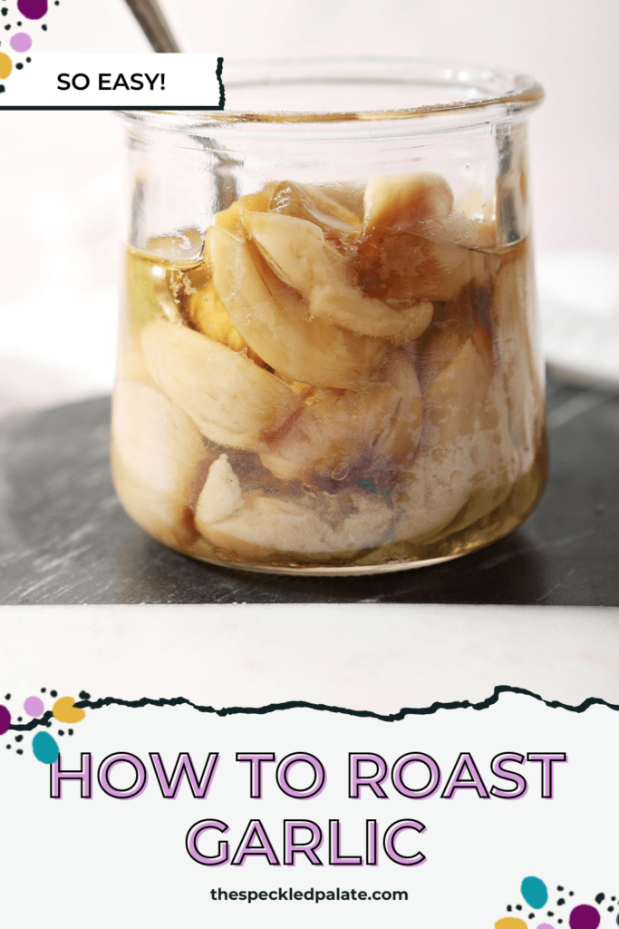 A jar of roasted garlic cloves with a spoon inside sits on black and white cutting board with the text how to roast garlic