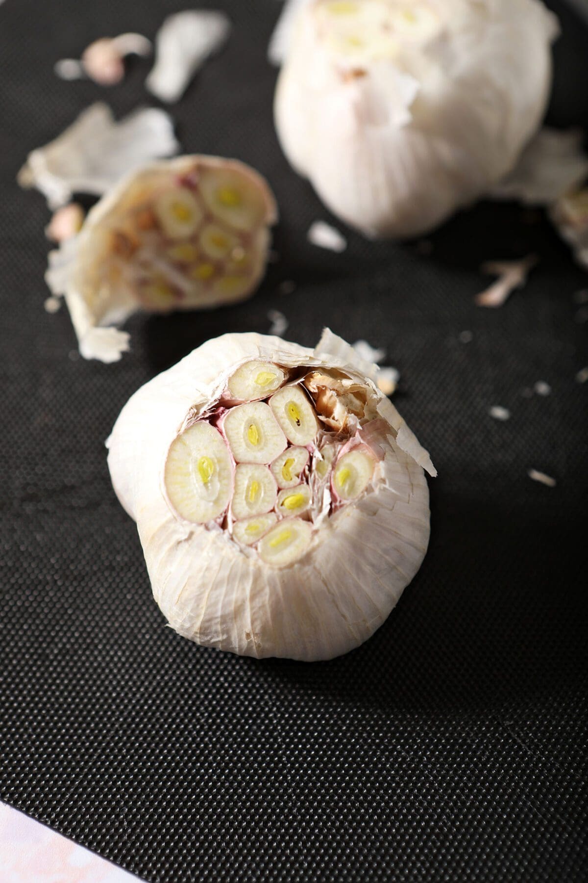 The top of a garlic clove is chopped off on a cutting board