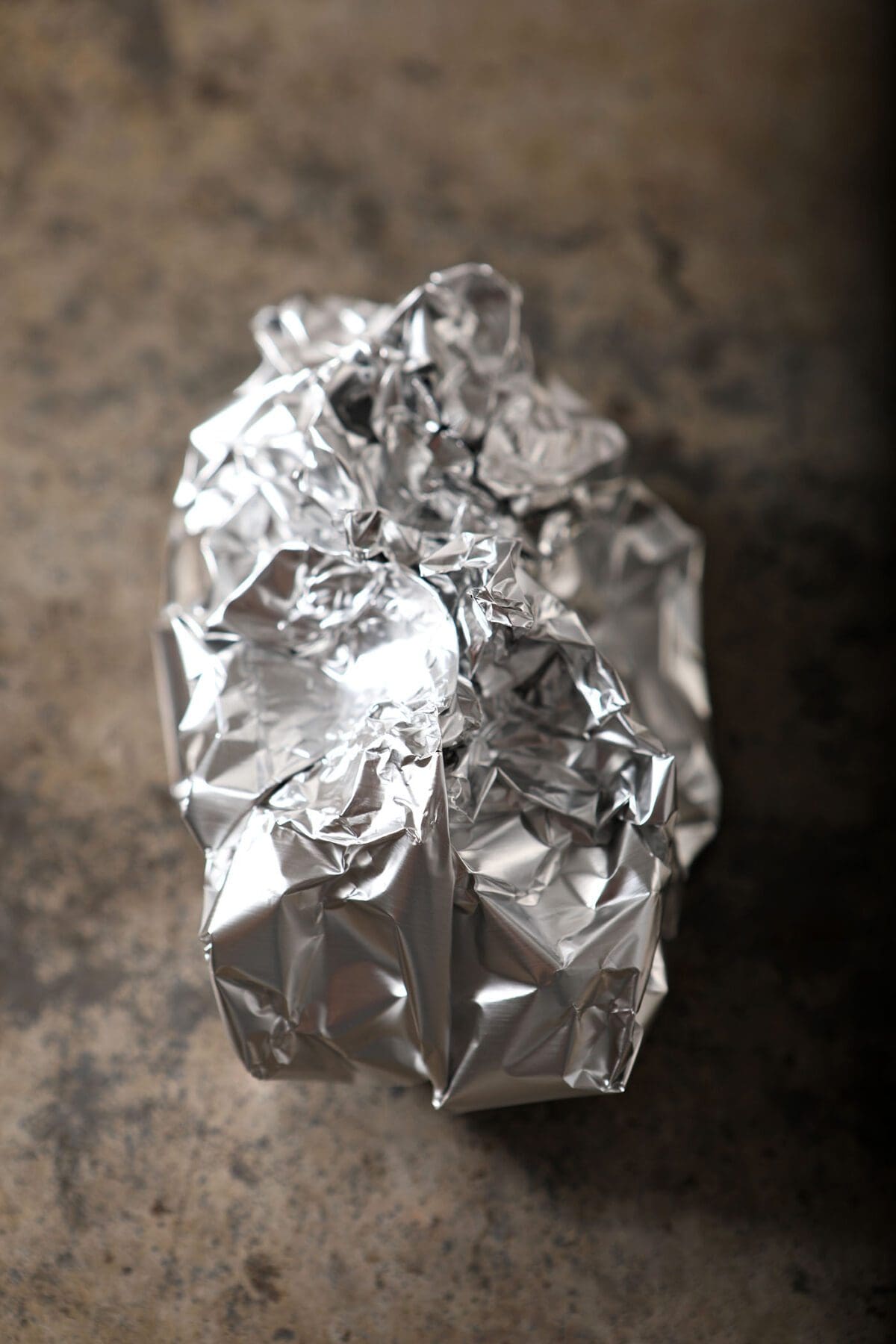 Garlic heads wrapped in foil on a sheet pan before baking