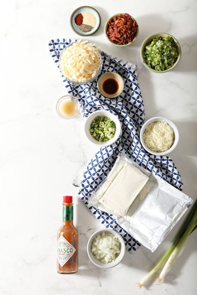 Ingredients to make a savory cheeseball recipe in bowls on a marble surface with a blue patterned towel