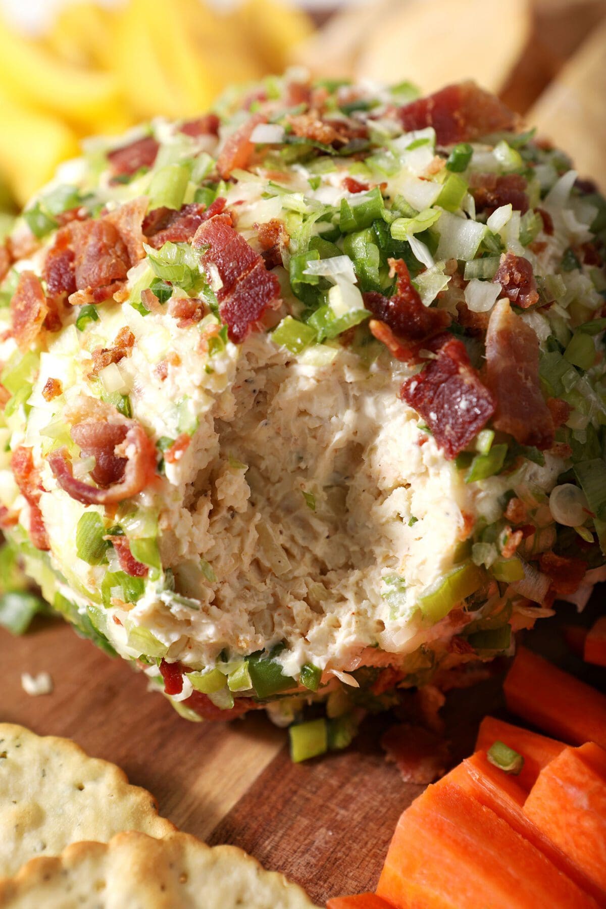 Close up of a cut-into cheeseball coated in green onions and bacon
