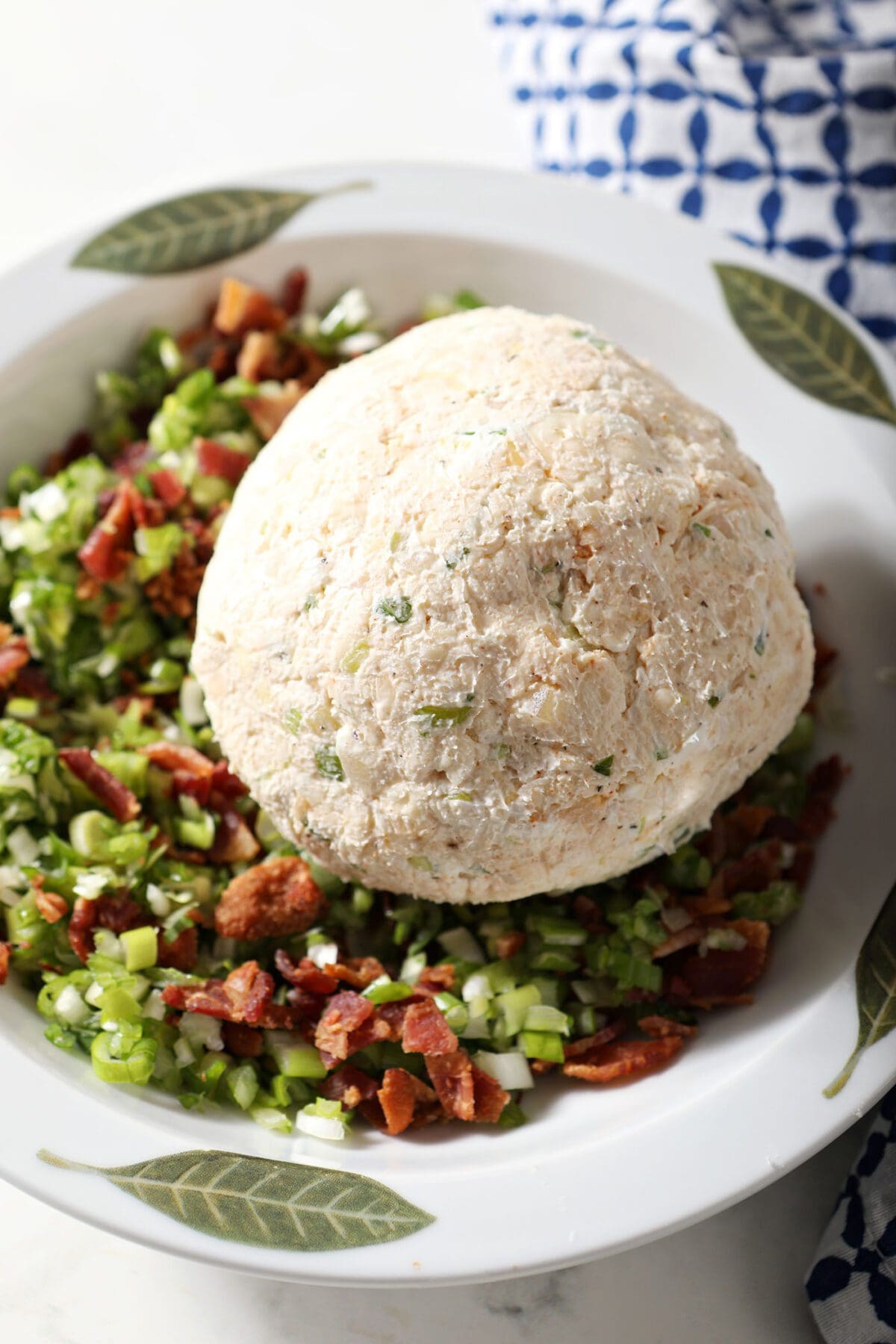 A cheeseball in a bowl of green onions and bacon crumbles