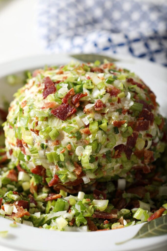 A cheeseball coated in green onion and bacon in a bowl before serving