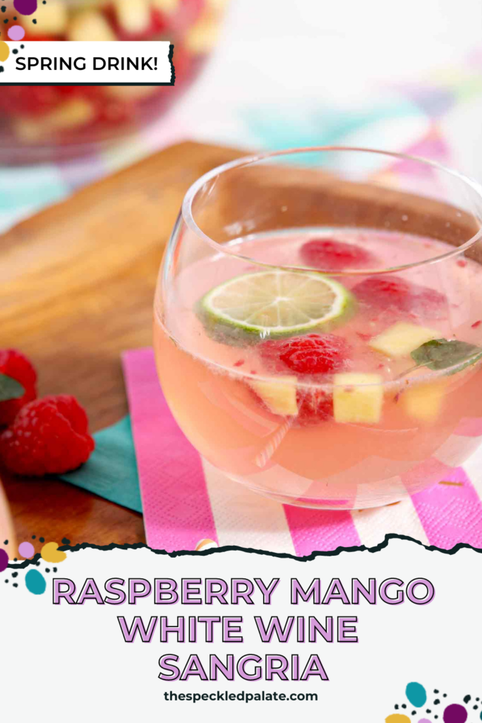 A glass of white wine sangria with raspberries and mango on a pink striped napkin with the text Raspberry Mango White Wine Sangria