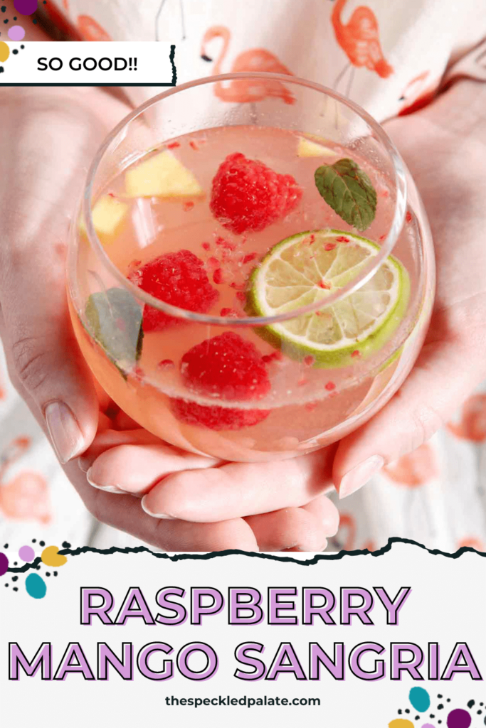 A woman in a flamingo shirt holds a glass of white wine sangria with mangos and raspberries floating in it with the text raspberry mango sangria