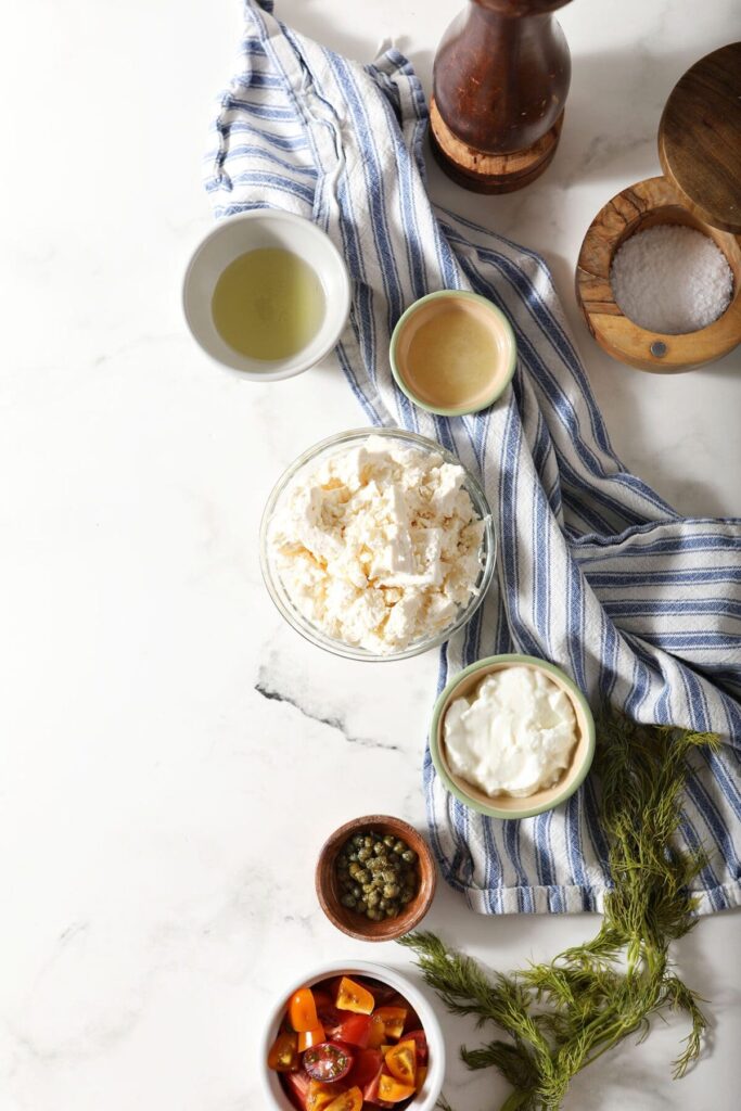 Ingredients to make feta dip recipe in bowls with a blue striped towel on marble