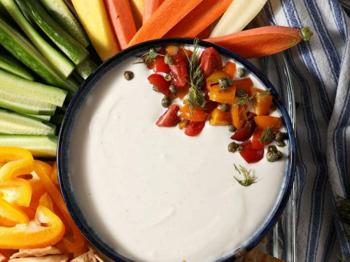 Whipped feta dip in a blue bowl garnished with tomatoes surrounded by raw vegetables and chips for dipping