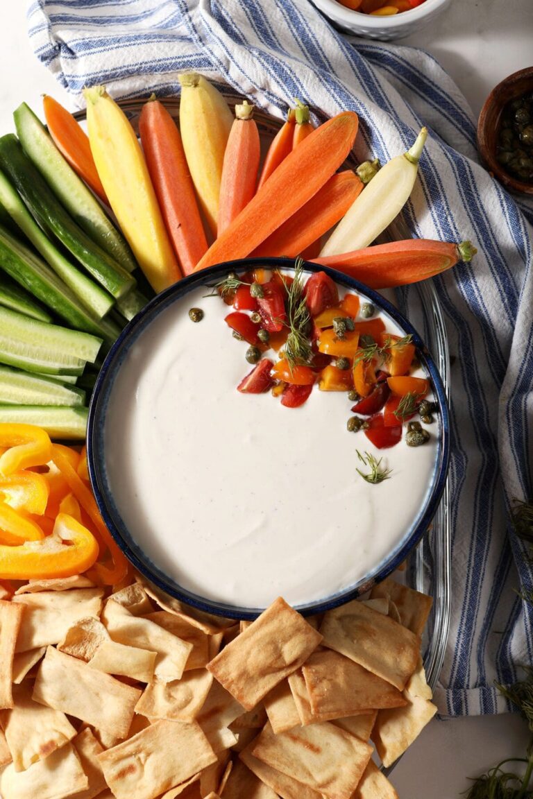 Whipped feta dip in a blue bowl garnished with tomatoes surrounded by raw vegetables and chips for dipping