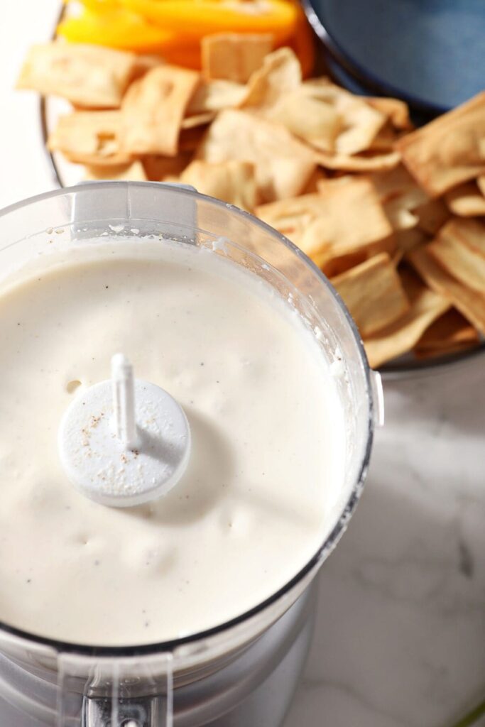 Smooth feta dip in a food processor next to a plate of chips