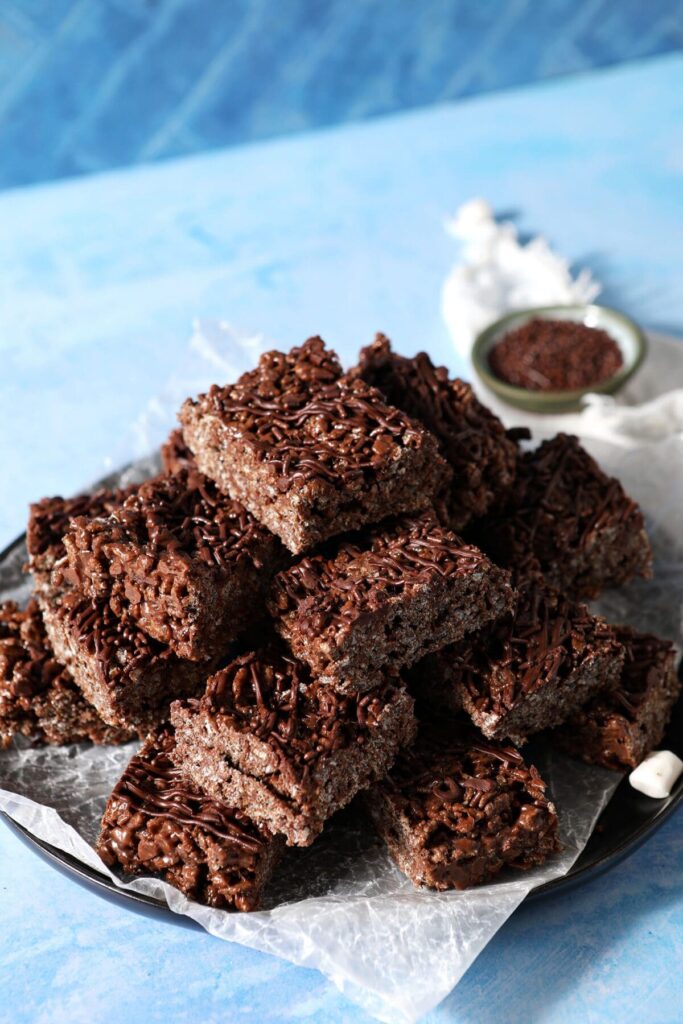 A platter of Chocolate Rice Krispie Treats stacked on top of each other on a blue surface