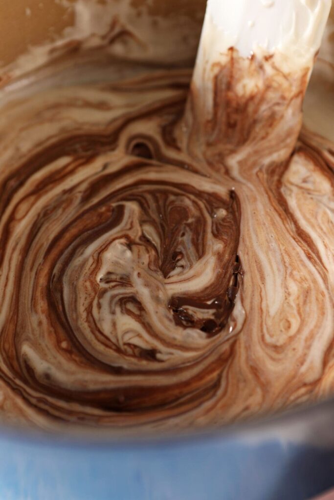 A rubber spatula swirls melted chocolate into a marshmallow mixture