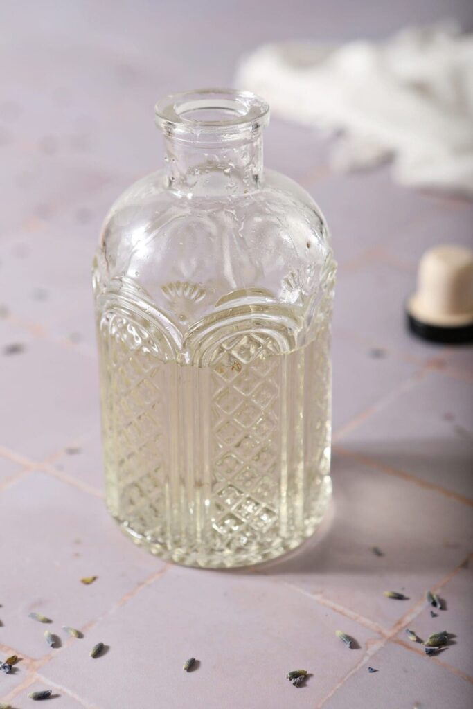 A bottle of lavender simple syrup with the lid off on a tiled purple surface