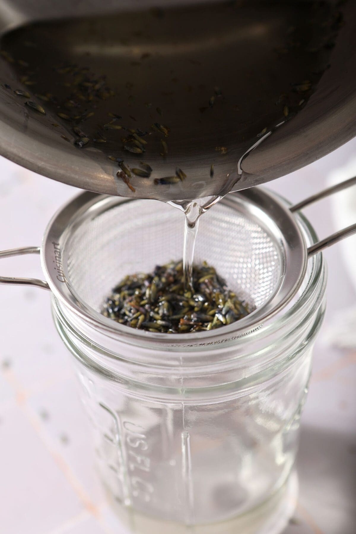 Lavender simple syrup pours through a fine mesh strainer above a mason jar