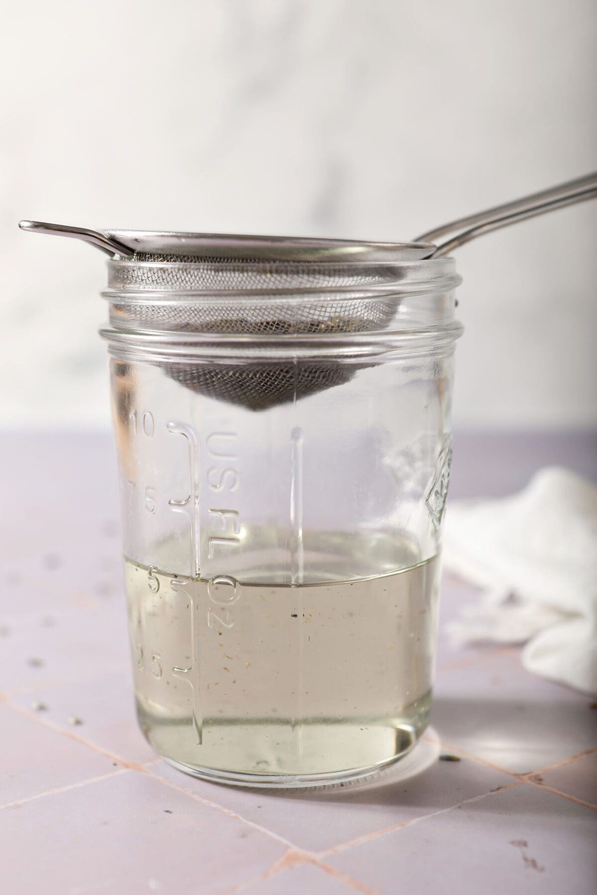 Lavender simple syrup is strained into a mason jar to catch the lavender flower buds